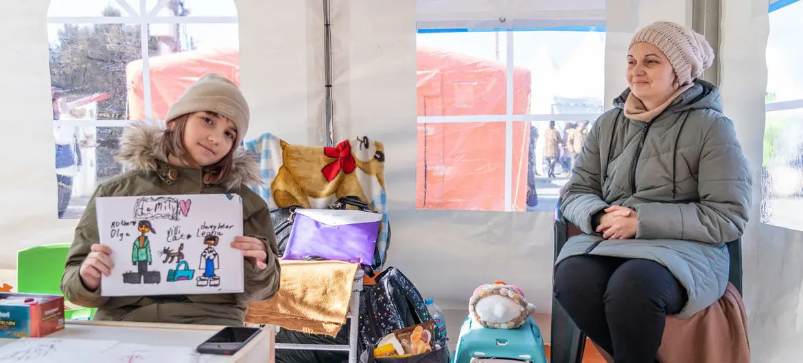 A nine-year-old Ukrainian girl holds a drawing of her family as she sits in a learning hub with her mohther and cat (in blue basket) in Romania. A nine-year-old Ukrainian girl holds a drawing of her family as she sits in a learning hub with her mohther and cat (in blue basket) in Romania.