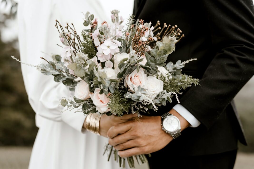 Brücke und Bräutigam stehen, während sie Blumenstrauß halten