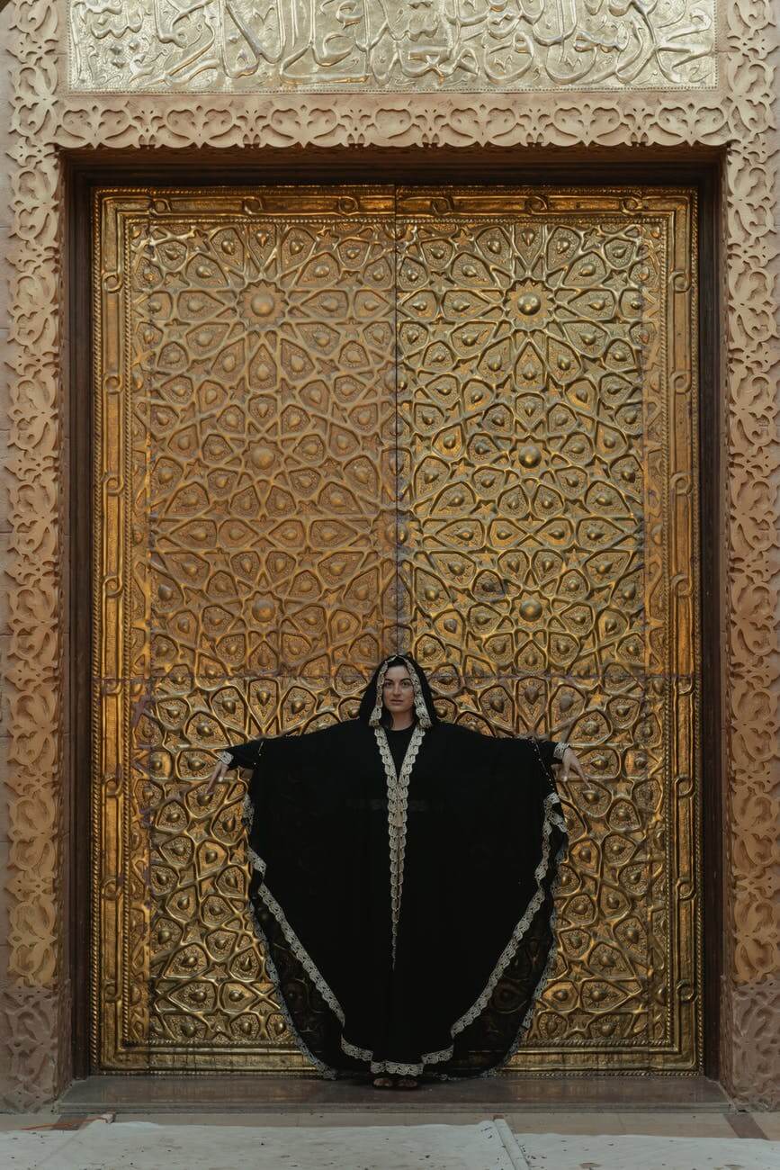 Frau in schwarzer Abaya, die neben einer goldenen Tür steht