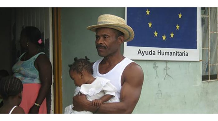 a man with a child in his arms behind him the EU flag with the words 