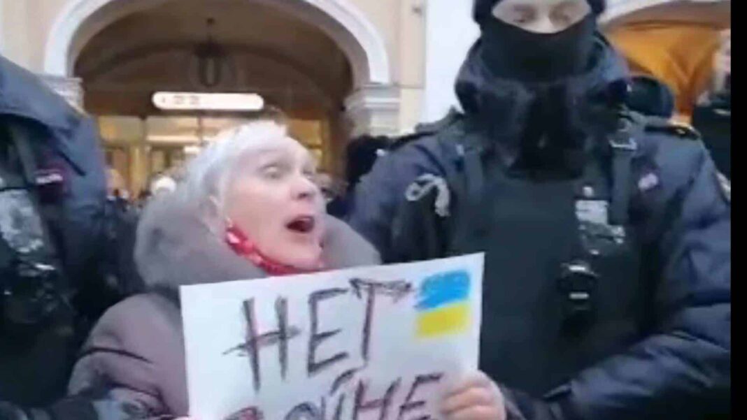 пожилая женщина с седыми волосами держит плакат против войны в Украине, задержанная двумя российскими полицейскими