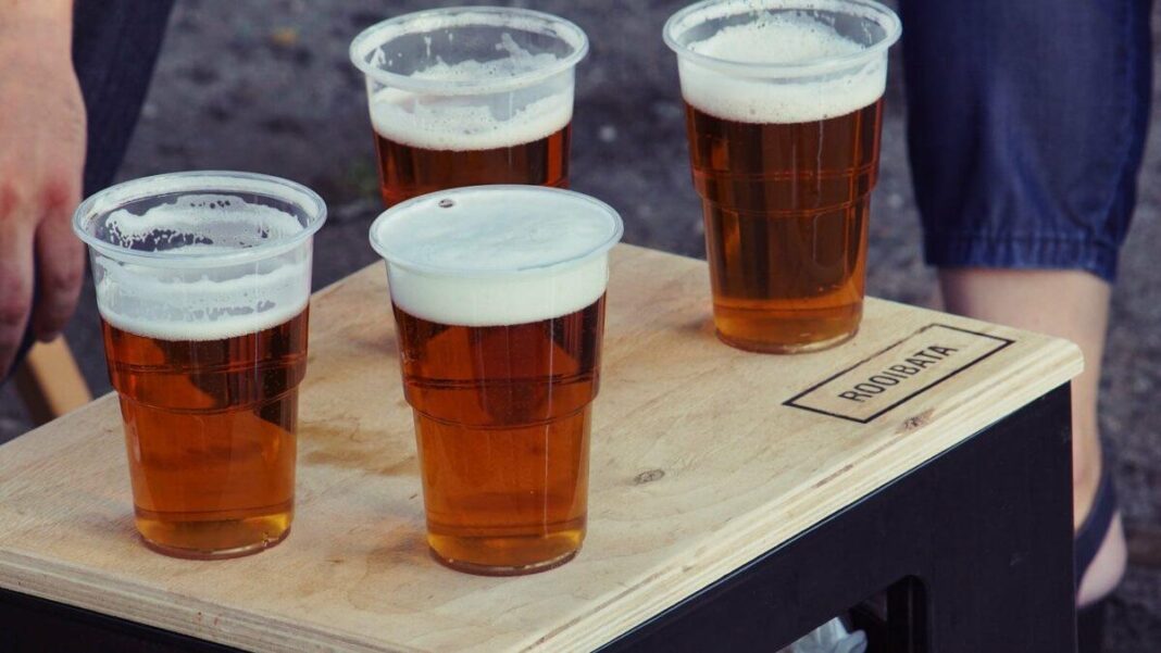 four clear plastic disposable cups with beer on the top of the board alcohol