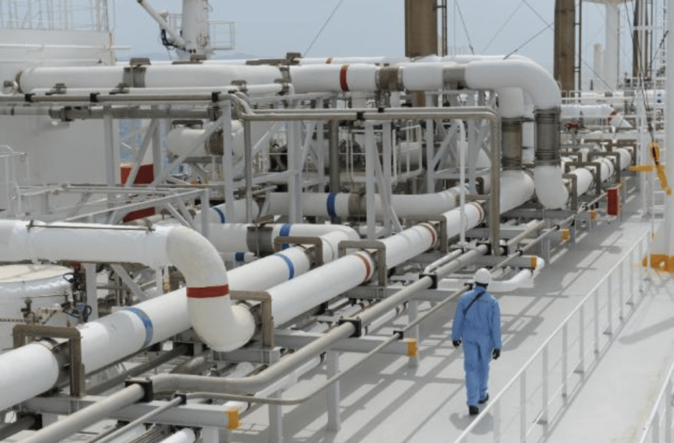 A crew member walking by a gas pipes network on a LNG tanker upper deck