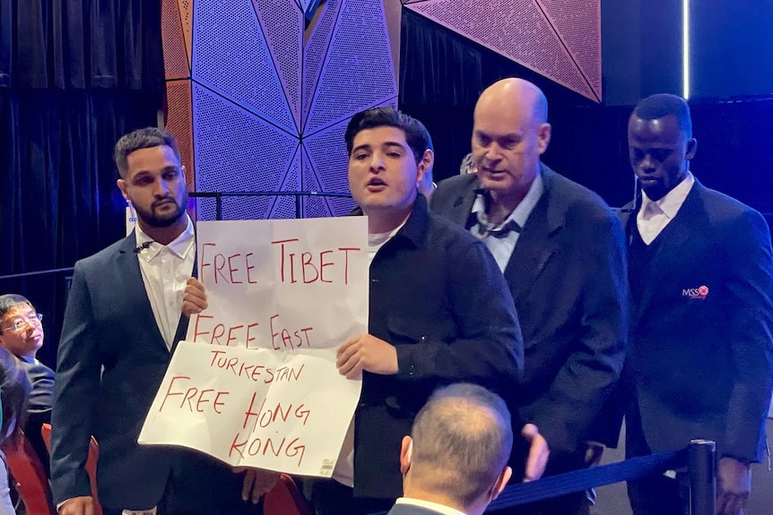 Activist Drew Pavlou holds sign and shouts Free Uyghurs during the ambassador Xiaos speech on Friday PhotoABC News Activists disrupt Chinese envoy’s speech in Australia