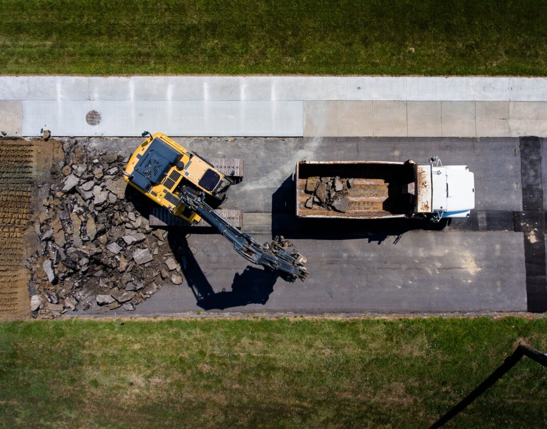 fotografia aérea de equipamento pesado amarelo ao lado do caminhão basculante branco durante o dia